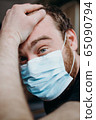 Sad balding adult man in a medical mask holding his head with his hands. 65090794