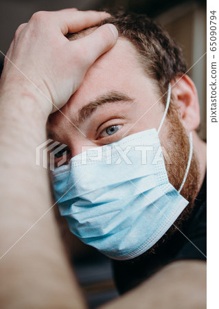 Sad balding adult man in a medical mask holding his head with his hands. Sad balding adult man in a medical mask holding his head with his hands. 65090794