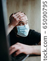 Coronavirus, an adult male with a beard works at a laptop. Protective respiratory mask. 65090795