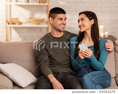 Couple using cell phone sitting on couch, free space Couple using cell phone sitting on couch, free space 65091879