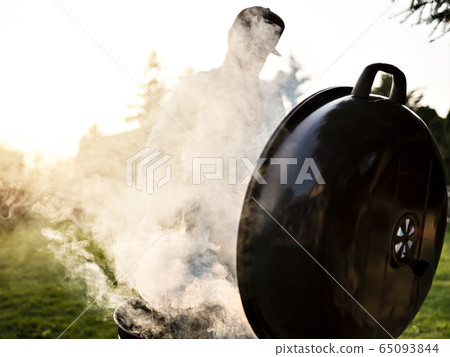 Unrecognisable man cooks meat outdoor. 65093844