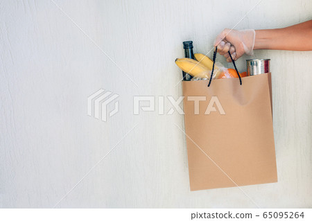 Paper bag with food in woman's hand wearing protective glove on the white wall in background. Paper bag with food in woman's hand wearing protective glove on the white wall in background. 65095264