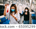 Young asian woman wearing protective face mask using smartphone in underground train 65095299