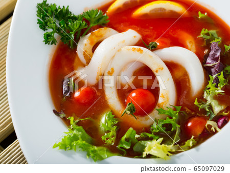 Spicy tomato soup with sea squids and greens served in a white bowl 65097029