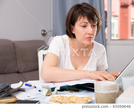 Woman with documents while working at laptop at home Woman with documents while working at laptop at home 65098646