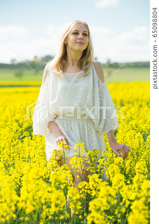 Girl posing in rape seed flowers field posing in white dress at sunny day Girl posing in rape seed flowers field posing in white dress at sunny day 65098804
