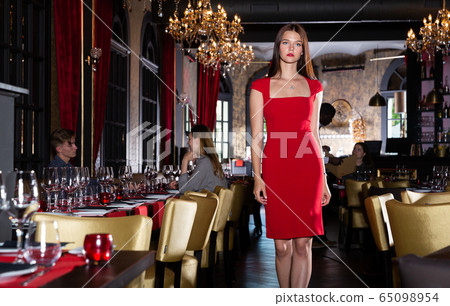 Attractive young woman in red dress walks through hall of a fashionable restaurant 65098954