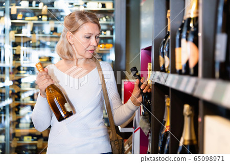 Portrait of mature woman visiting winehouse in search of bottle of good wine Portrait of mature woman visiting winehouse in search of bottle of good wine 65098971