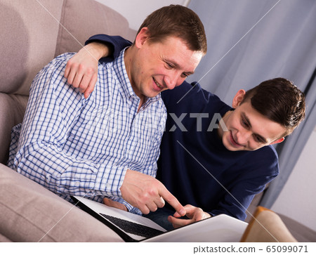 Man with his adult son are playing on laptop together 65099071