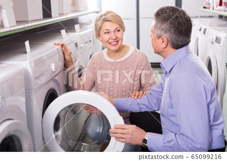 attentive mature couple chooses washing machine for their house in shop of household appliances attentive mature couple chooses washing machine for their house in shop of household appliances 65099216