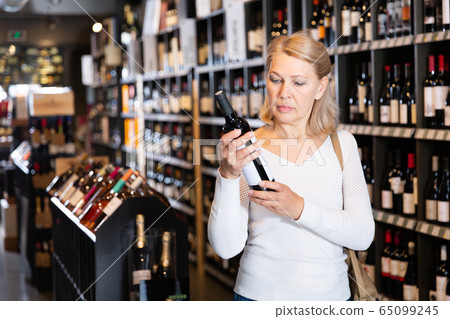Woman choosing bottled wine in wineshop 65099245