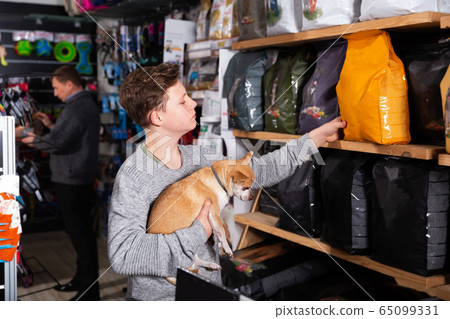 Teenager with dog choosing food in petshop Teenager with dog choosing food in petshop 65099331