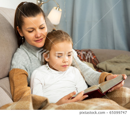 Young woman reading an interesting book with daughter Young woman reading an interesting book with daughter 65099747
