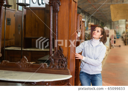 Cheerful woman buyer standing in furniture shopping room near wardrobe Cheerful woman buyer standing in furniture shopping room near wardrobe 65099833