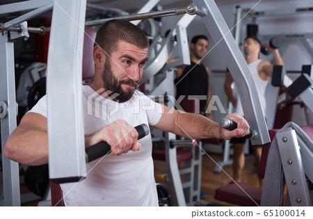 Guy training on fitness machine in gym Guy training on fitness machine in gym 65100014