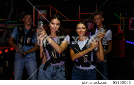 Two young women standing with guns during laser tag game with men Two young women standing with guns during laser tag game with men 65100096