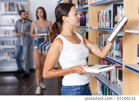 Female student choosing necessary books on shelves in library Female student choosing necessary books on shelves in library 65100232