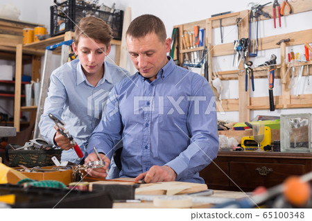 father and teen son working with wood plank in workshop father and teen son working with wood plank in workshop 65100348