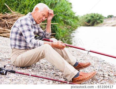 Aged man fishing at lakeside 65100417