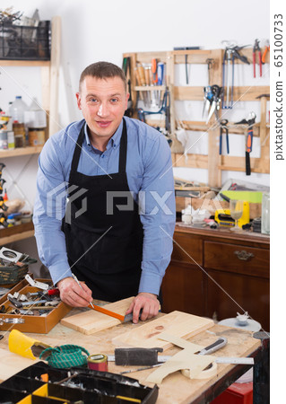 woodwork studio with shelving holding pieces of wood, with a carpenter standing in his workbench woodwork studio with shelving holding pieces of wood, with a carpenter standing in his workbench 65100733