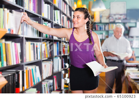 Female is choosing interesting book 65100923