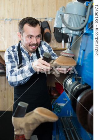 Man worker repairing shoes in repair workshop 65100971