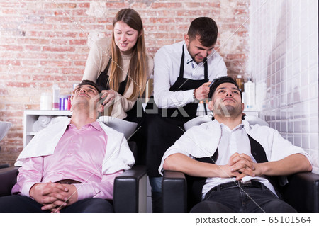 Men relaxing while hairdressers washing their hair 65101564