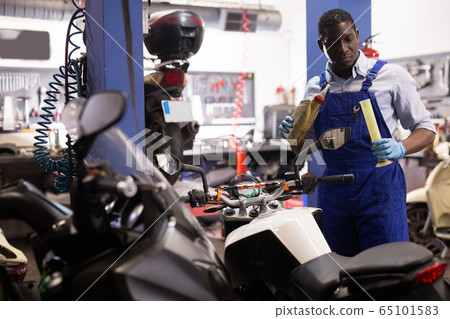Engineer in overalls pours oil for motorcycle engine in garage 65101583