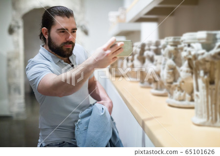 Adult male visitor using phone in sculptures exposition at museum Adult male visitor using phone in sculptures exposition at museum 65101626
