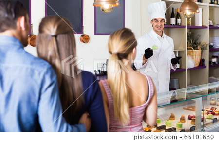 Male pastry chef helping customers to choose sweets Male pastry chef helping customers to choose sweets 65101630