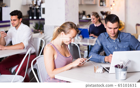 Young smiling woman with boyfriend busying with device in modern cafe Young smiling woman with boyfriend busying with device in modern cafe 65101631