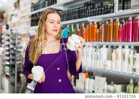 Focused interested girl shopping in cosmetics store looking for hair care treatments 65101726