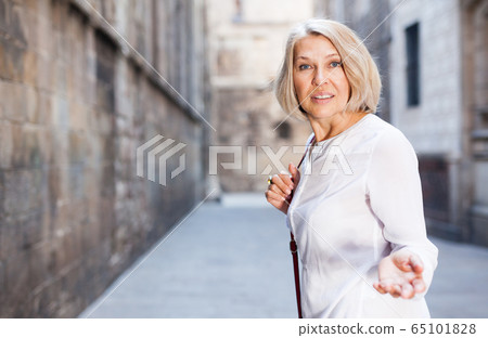 Portrait of mature positive woman welcoming the historical city center 65101828