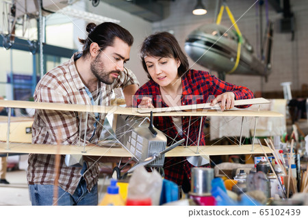 Positive couple enjoying their hobbies - modeling light airplanes in aircraft hangar Positive couple enjoying their hobbies - modeling light airplanes in aircraft hangar 65102439