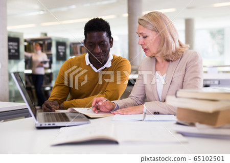Female teacher working with african-american man in university library Female teacher working with african-american man in university library 65102501