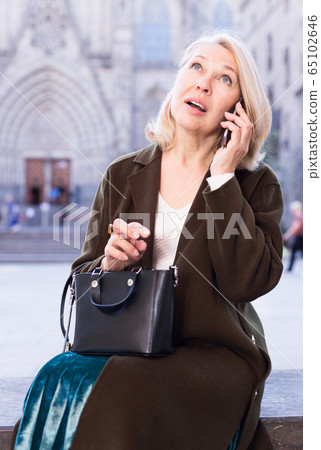 Mature positive female talking on phone in the historical city center 65102646
