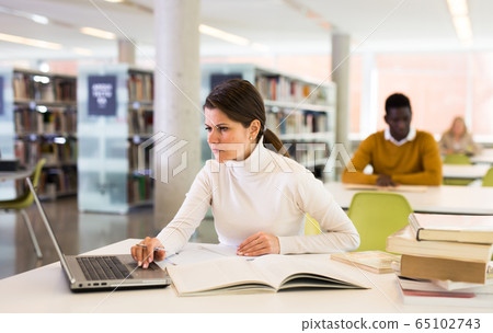 Adult female student with laptop and books in public library 65102743