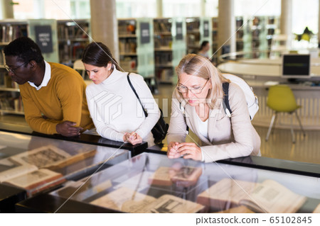 Teacher and adult students view rare books in a library showcase Teacher and adult students view rare books in a library showcase 65102845