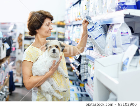 Careful senior woman visiting pet shop in search of dry food for her dog 65102900