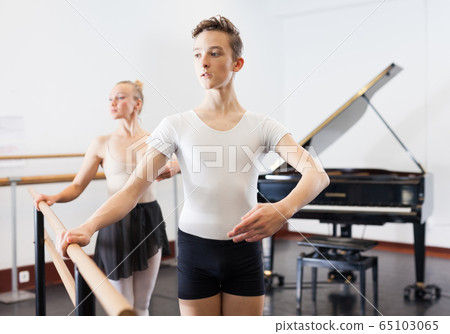 Choreographer woman and young man do exercises at ballet bar in hall with mirror Choreographer woman and young man do exercises at ballet bar in hall with mirror 65103065