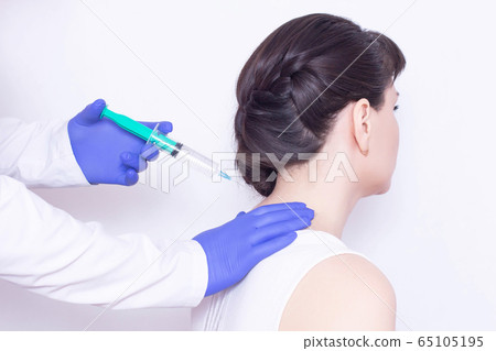 The doctor makes an injection of chondroprotector and anesthetic in the cervical vertebrae of the girl to eliminate pain and stiffness, inflammation, close-up 65105195