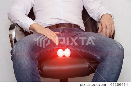 A man in a white shirt is sitting on a chair with a cyst of the epididymis of the scrotum, orchitis and inflammation, pain A man in a white shirt is sitting on a chair with a cyst of the epididymis of the scrotum, orchitis and inflammation, pain 65106414