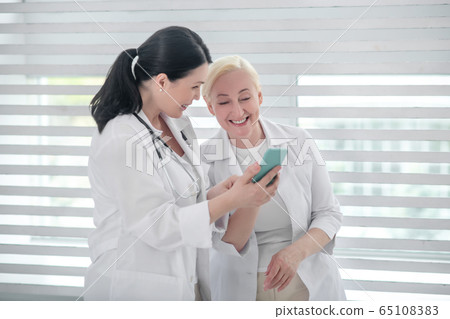 Two women in white coats standing near the window. Two women in white coats standing near the window. 65108383