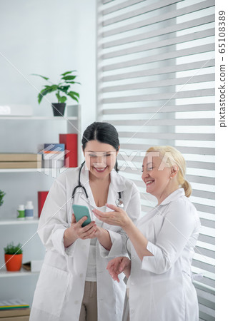 Two doctors in white robes watching a video together Two doctors in white robes watching a video together 65108389