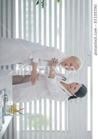Two doctors in white robes laughing together and looking happy Two doctors in white robes laughing together and looking happy 65108390