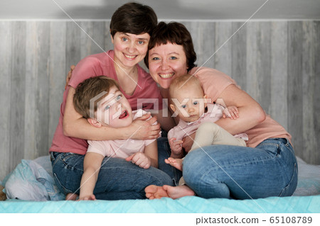 A young homosexual lesbian couple with two children at home, on the bed. A young homosexual lesbian couple with two children at home, on the bed. 65108789