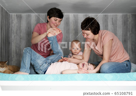 A young homosexual lesbian couple with two children at home, on the bed. A young homosexual lesbian couple with two children at home, on the bed. 65108791