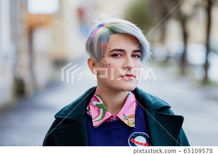 Portrait of a young beautiful woman with a short haircut and dyed hair. Grey main color and yellow, green, blue and red hair color. Portrait of a young beautiful woman with a short haircut and dyed hair. Grey main color and yellow, green, blue and red hair color. 65109578