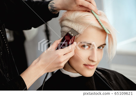 Hairdresser machine cuts woman client. A short haircut, shaved temple and a drawing on the hair. 65109621
