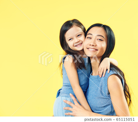 Happy mother and her child daughter hugging on yellow background. Happy mother and her child daughter hugging on yellow background. 65115051